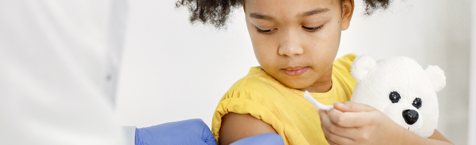 Little girl, holding teddy bear, getting an immunization.