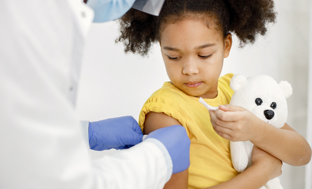 Small girl, holding teddy bear, receiving an immunization.