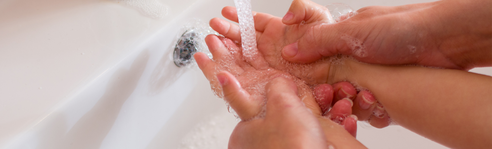 Child washing hands with adult assistance.